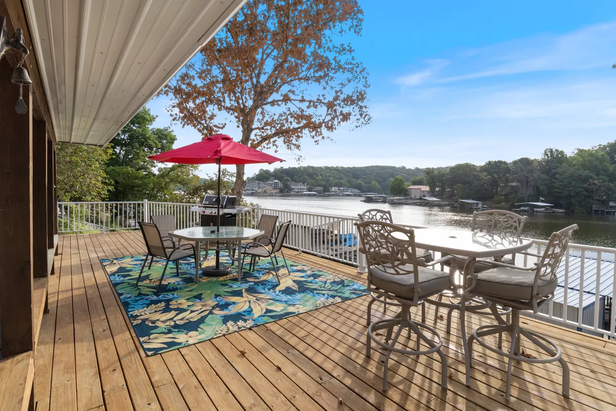 A welcoming outdoor dining area furnished with a colorful umbrella, comfortable chairs, and a textured area rug, all overlooking the tranquil lake. The setting suggests relaxation and the enjoyment of nature.