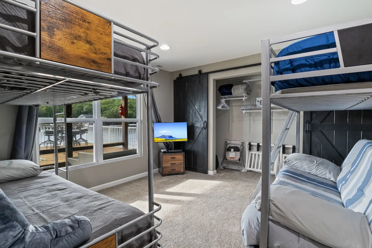 A vibrant, kid-friendly bedroom with bunk beds, a television, a large window, and a sliding barn door. The playful atmosphere invites children to sleep, watch TV, or socialize in a cozy space that's clearly designed with families in mind.