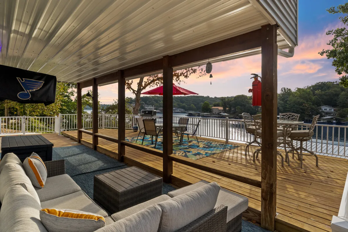 A comfortable exterior seating and dining area with a decorative rug, all set against a stunning lake backdrop. The spacious setting invites both relaxation and group gatherings, enhancing the sense of indoor-outdoor flow.