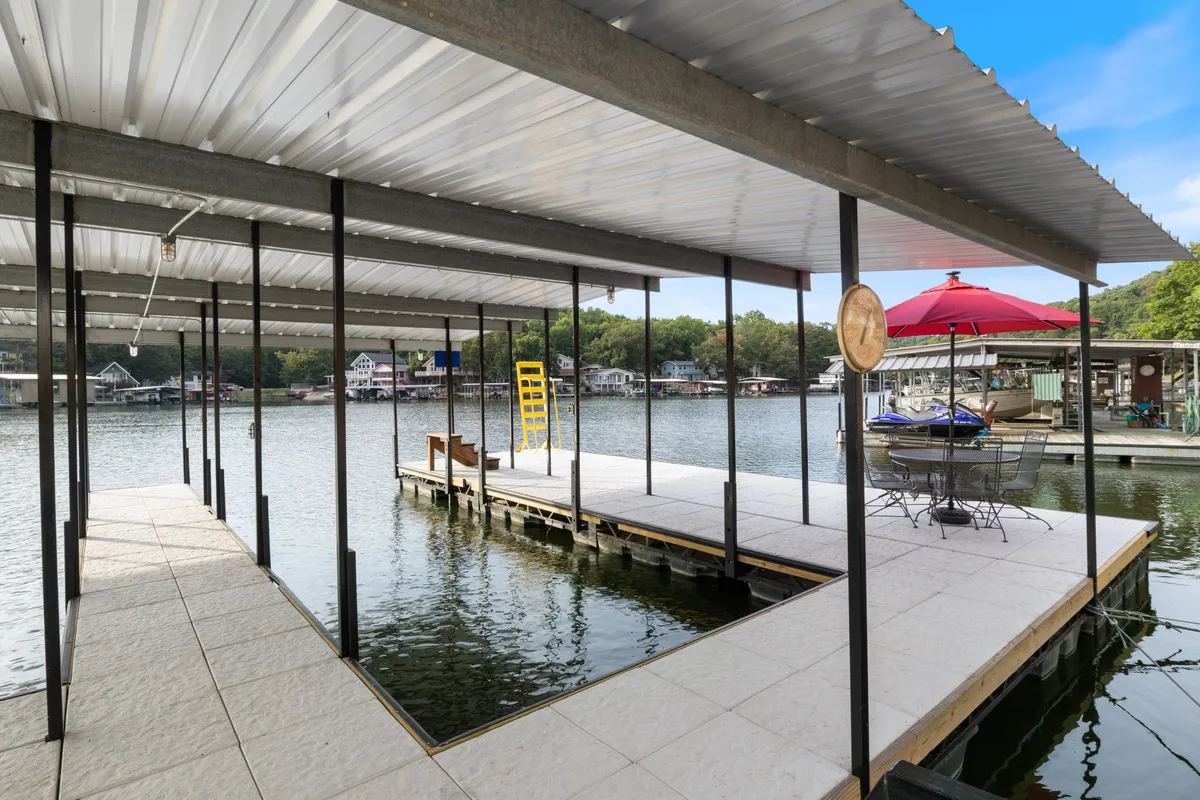 A tranquil boat dock with a large umbrella and comfortable seating area overlooking the water. The dock extends into the lake, perfect for fishing, relaxing, or supervising water activities. Lush greenery and open views create a relaxed, inviting setting.
