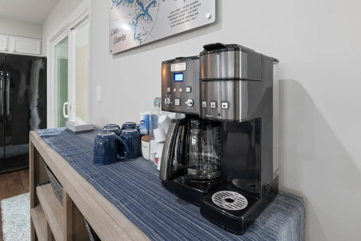 A close-up view of the kitchen’s coffee and beverage setup, featuring a modern coffee maker, blue mugs, and cozy decor. The space feels intimate and thoughtfully stocked, inviting guests to start their day with a hot drink while taking in the lakeside ambiance.