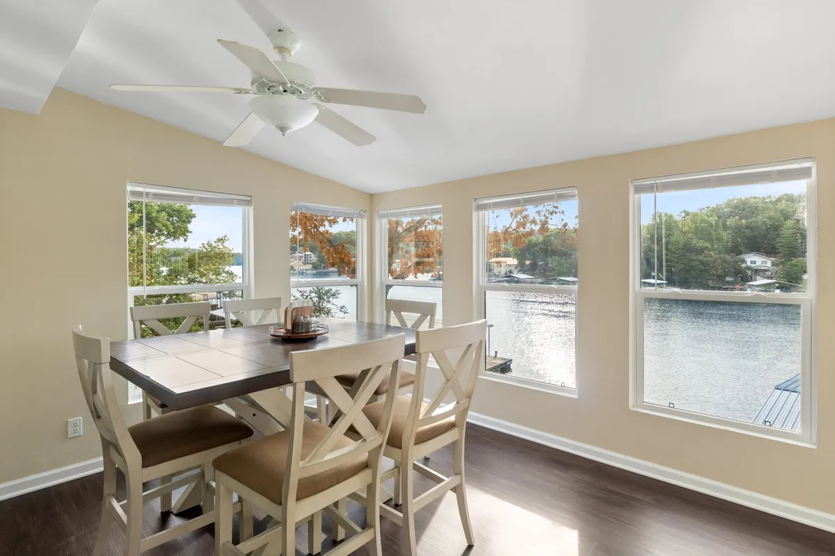A bright dining area with a large table positioned next to expansive windows, offering unobstructed views of the water. The calm, welcoming mood is enhanced by natural light, and the setting is perfect for family meals or board games with a view of the lake.