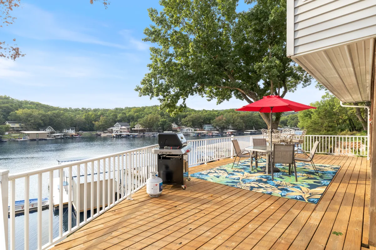 An inviting outdoor setting featuring a grill, a dining table set beneath a vibrant red umbrella, and a sweeping view of the lake. The scene evokes a sense of relaxation, celebration, and connection with the outdoors—ideal for morning coffee or evening gatherings with loved ones.