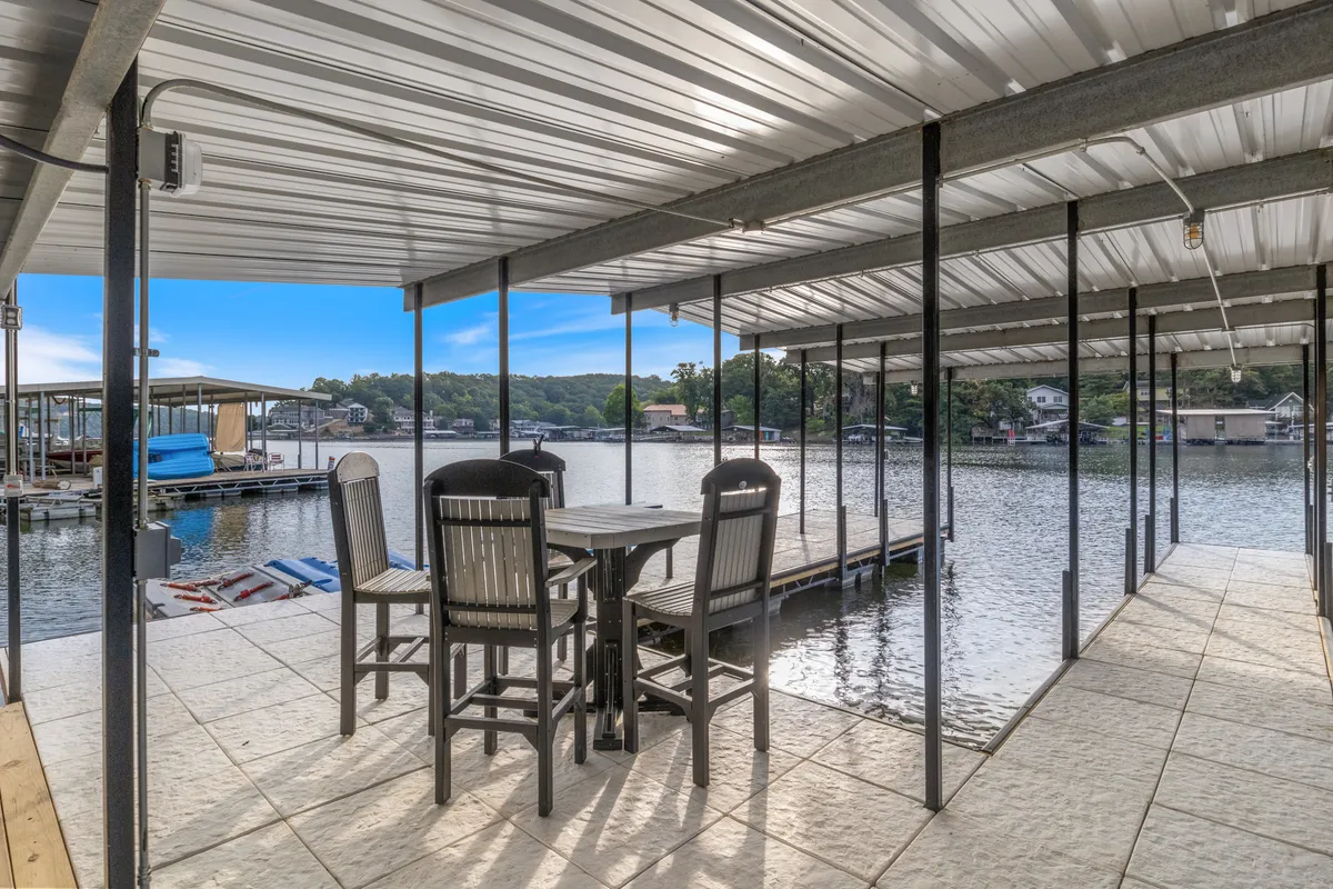 A serene outdoor dining set overlooks the water, with a visible dock area perfect for fishing, paddleboarding, or simply enjoying the tranquil setting. The space is designed for both dining and lake activities, encouraging play and relaxation.
