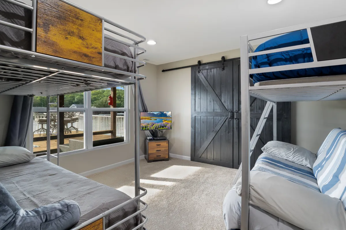 A playful bedroom designed for family convenience, featuring bunk beds, a television, and a sliding barn door. The setup is ideal for kids or group stays, with room for relaxation, play, and togetherness.