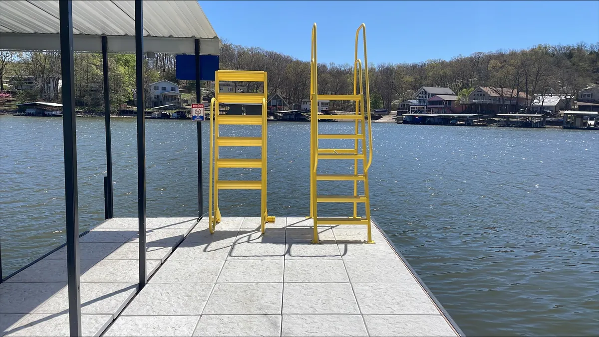 This exterior image highlights yellow ladders leading into calm lake water from a private dock area, ideal for swimming or launching water activities. The docking platform is visible, suggesting ample space for sunbathing, relaxing, or prepping gear for a day on the lake.