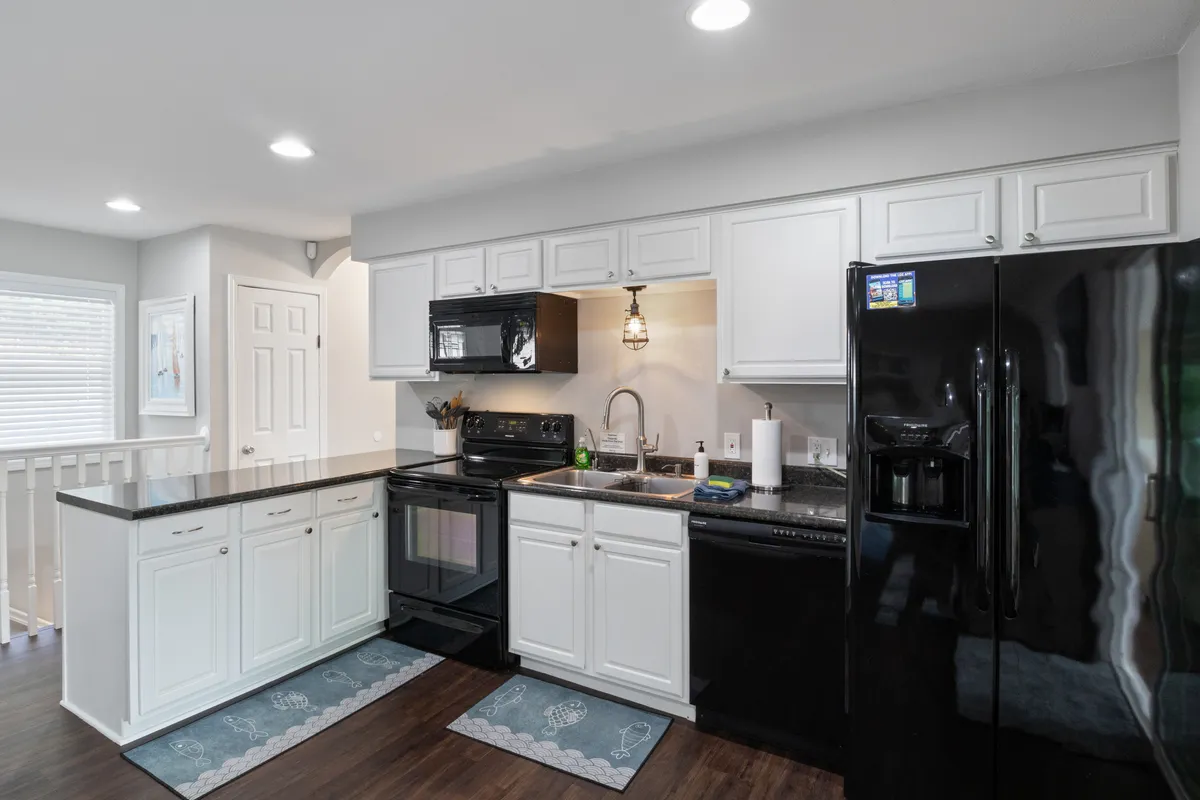 A warm, welcoming kitchen space with a large granite island, black appliances, and pendant lighting. The layout emphasizes ample workspace and storage, ideal for preparing group meals or morning breakfasts. The setting feels both functional and inviting, ready for any culinary occasion.